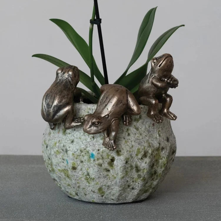 Three resin frog planter hangers on speckled pot with green stems