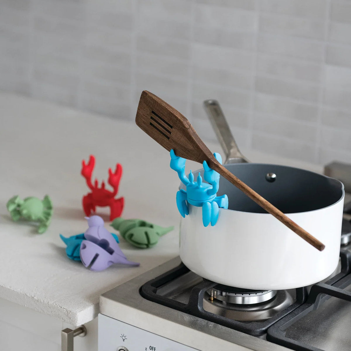Silicone crab-shaped lid/spoon holder in blue, resting across a pot