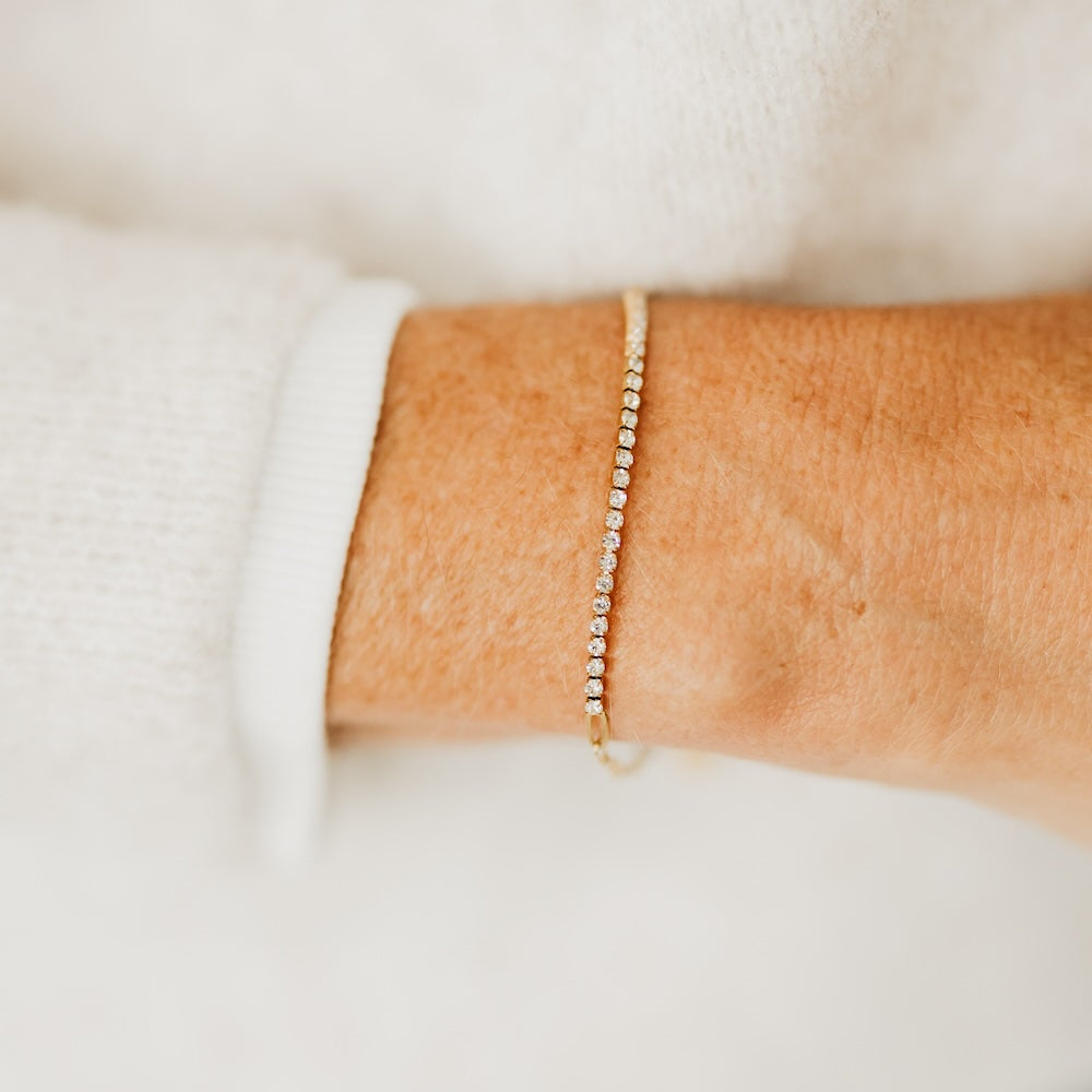 Gold-tone tennis chain bracelet with small clear stones, worn on wrist