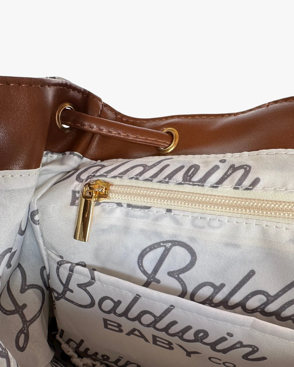 Diaper bag interior close-up with branded lining, zip pocket, and gold-tone hardware
