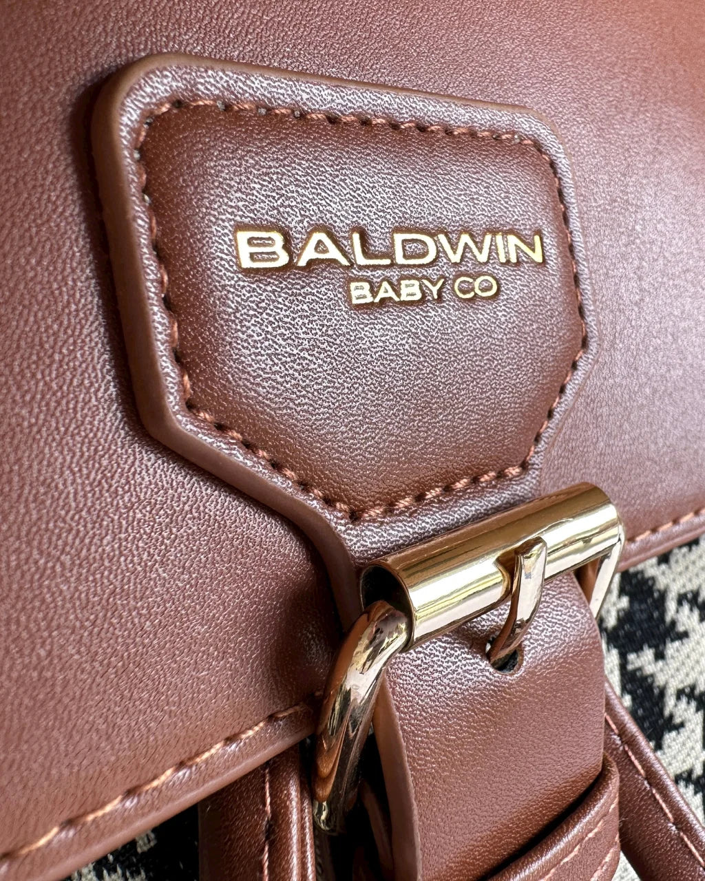 Close-up of the brown diaper bag flap, gold-tone clasp, and Baldwin Baby Co. logo