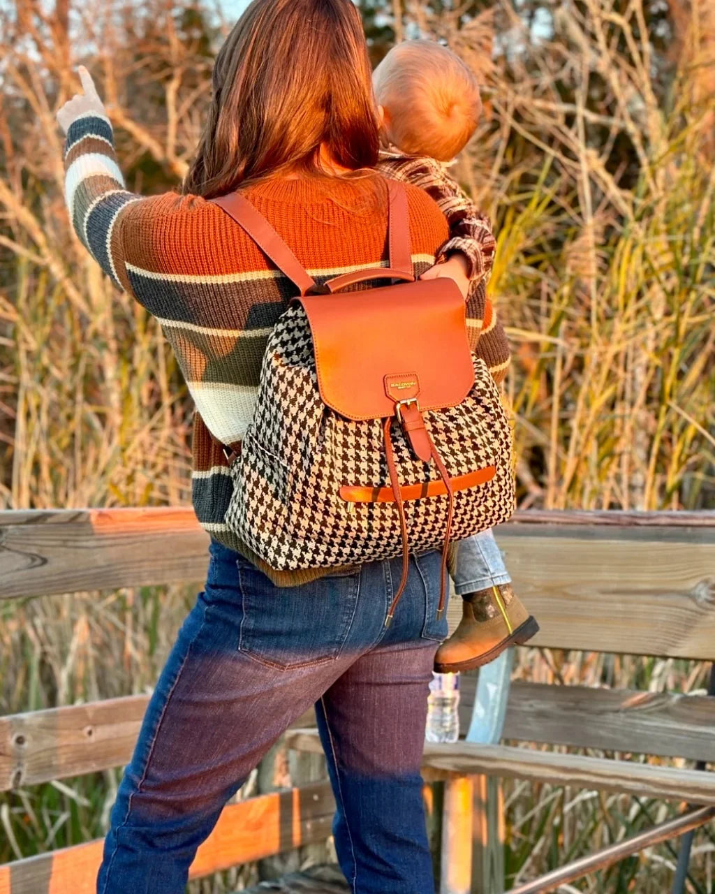 Houndstooth diaper bag worn as a backpack with brown flap and drawstring details