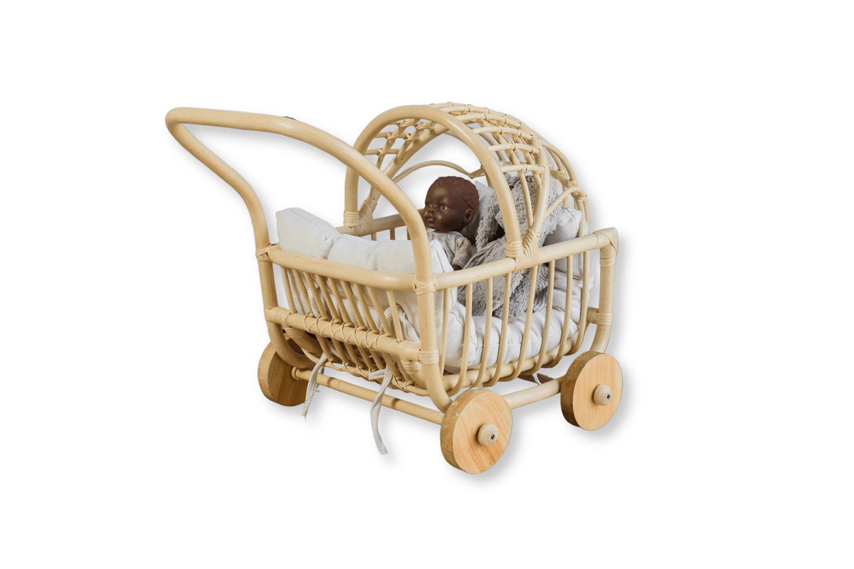 Angled view of natural rattan doll pram with white cushions, arched canopy, and wooden wheels