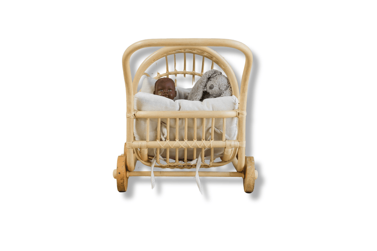 Front view of rattan doll stroller with white bedding and dolls nestled beneath the canopy