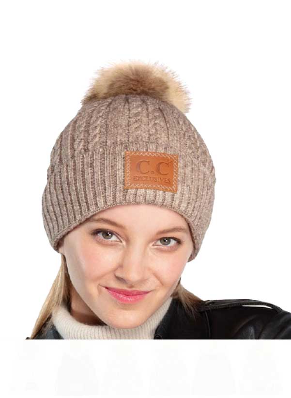 Taupe ribbed knit beanie with faux fur pom-pom and front logo patch, worn