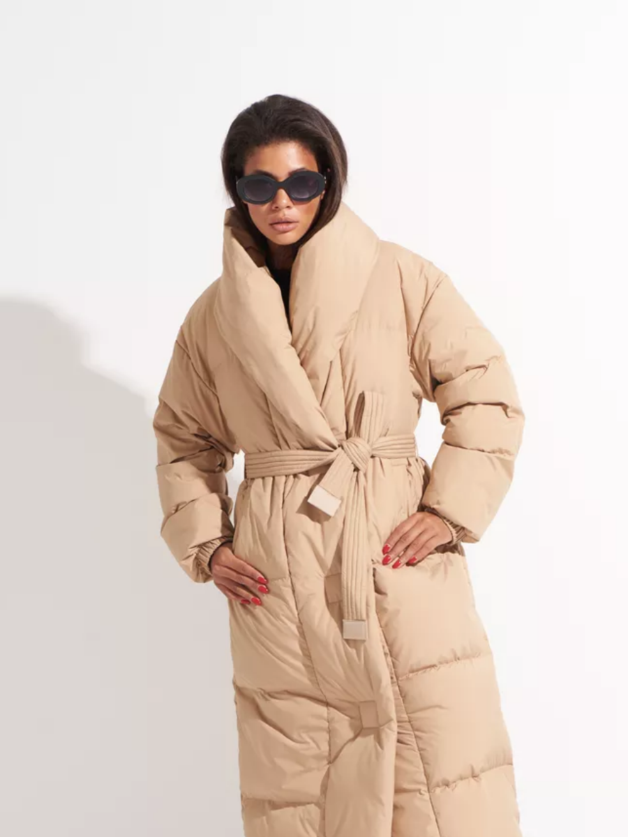 Long caramel down coat with a wide shawl collar, quilted sleeves and a belted waist.