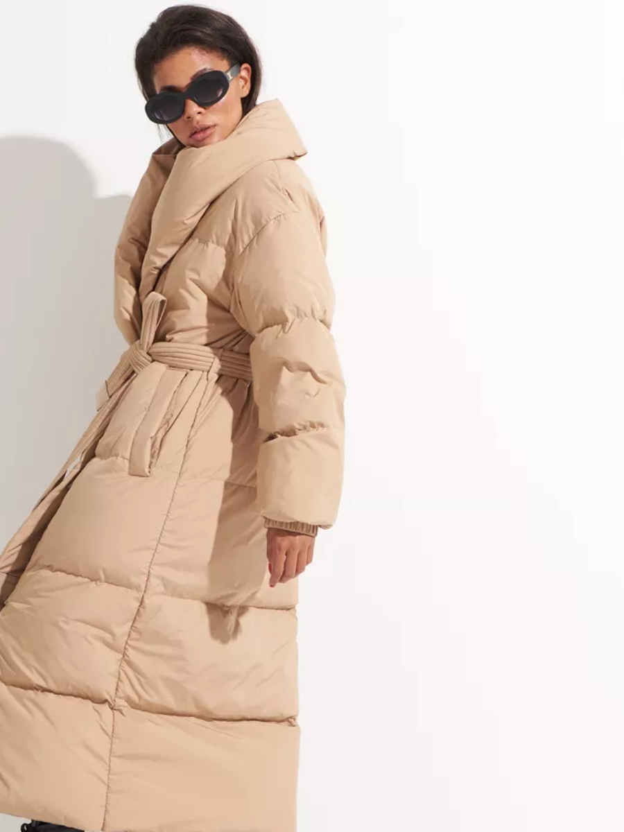 Caramel insulated down coat with a long hem, quilted panels, shawl collar and tied belt.