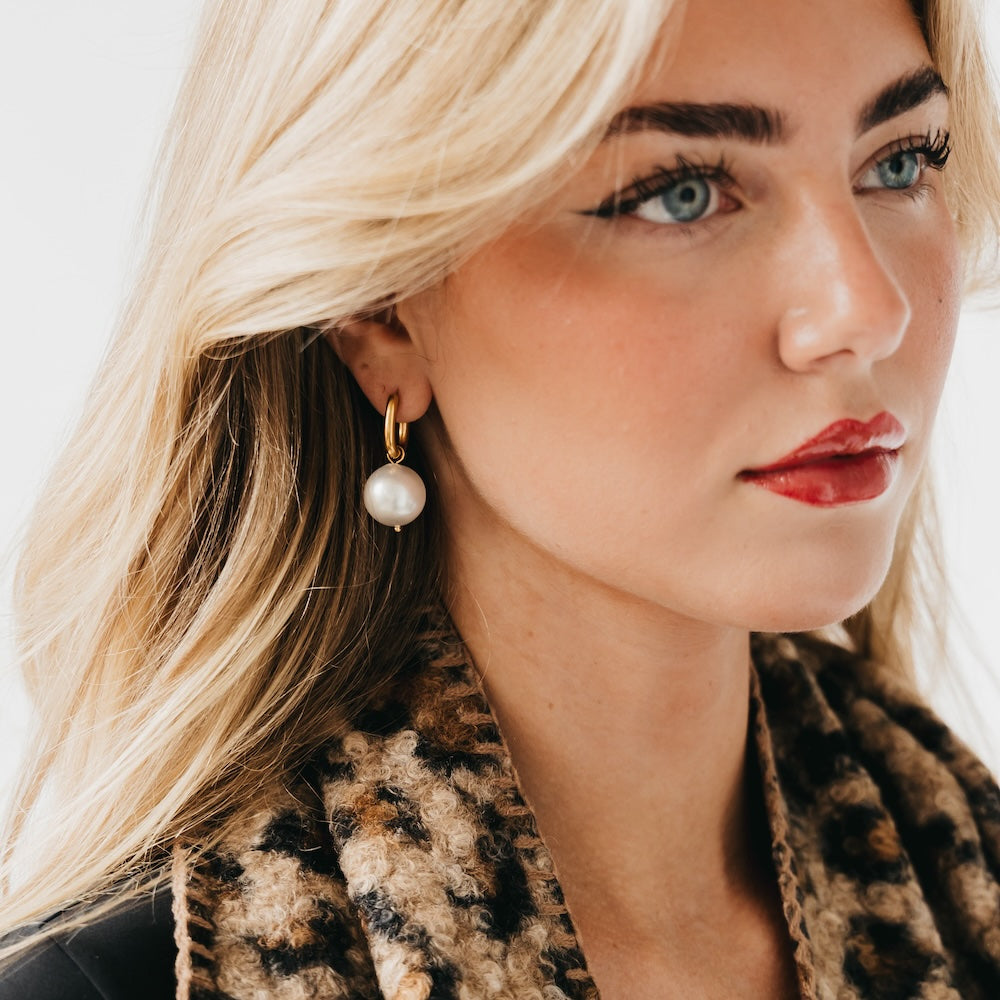 Gold-tone huggie hoop earrings with white pearl drop, on model