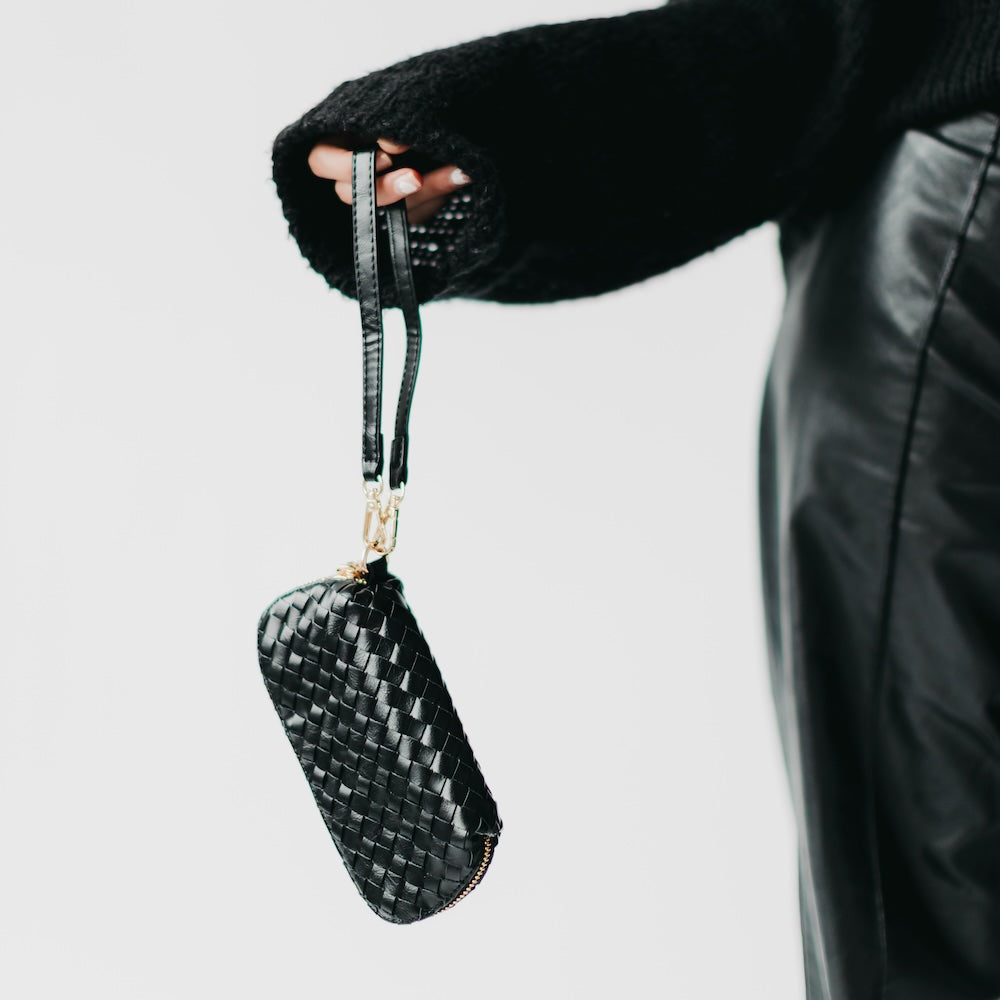 Woven black sunglass case wristlet hanging from strap with gold hardware