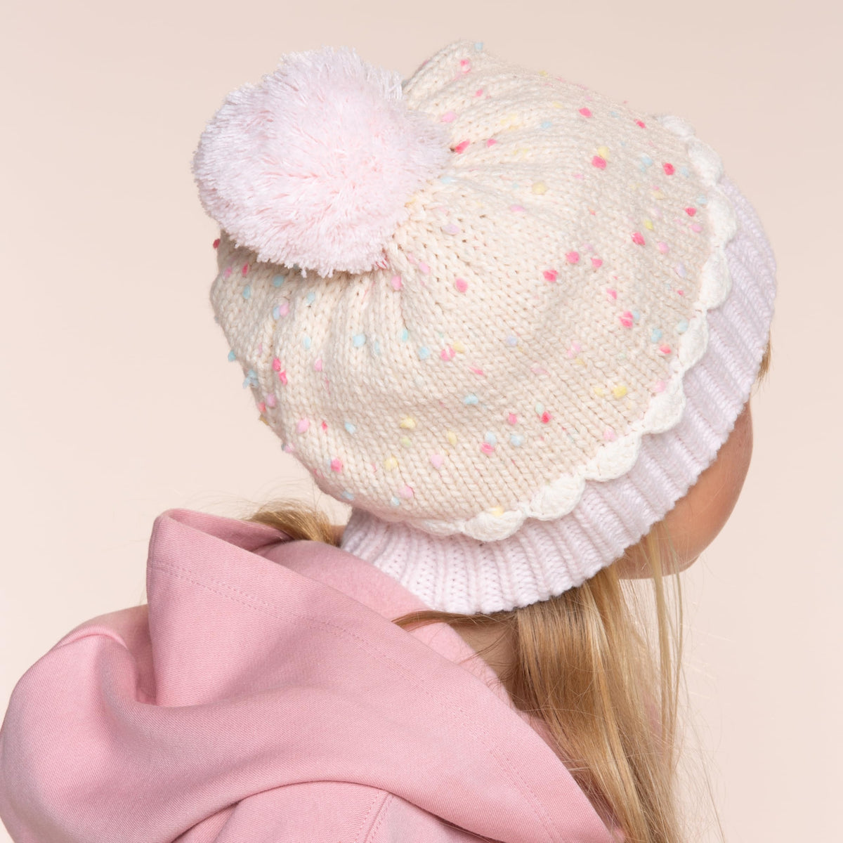 Back view of child wearing a pale speckled knit beanie with pom-pom and ribbed cuff