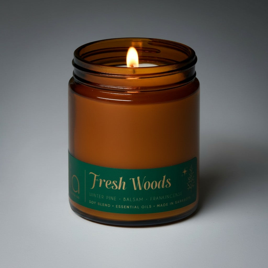Amber glass Fresh Woods candle jar with green label and single lit flame