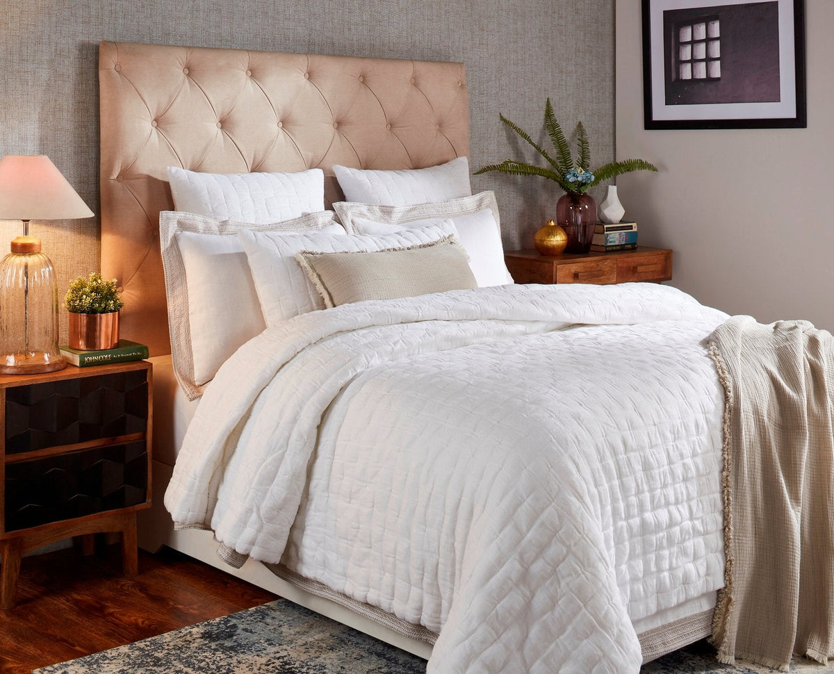 White pinched linen quilt covering a bed, with quilted center panel and layered look