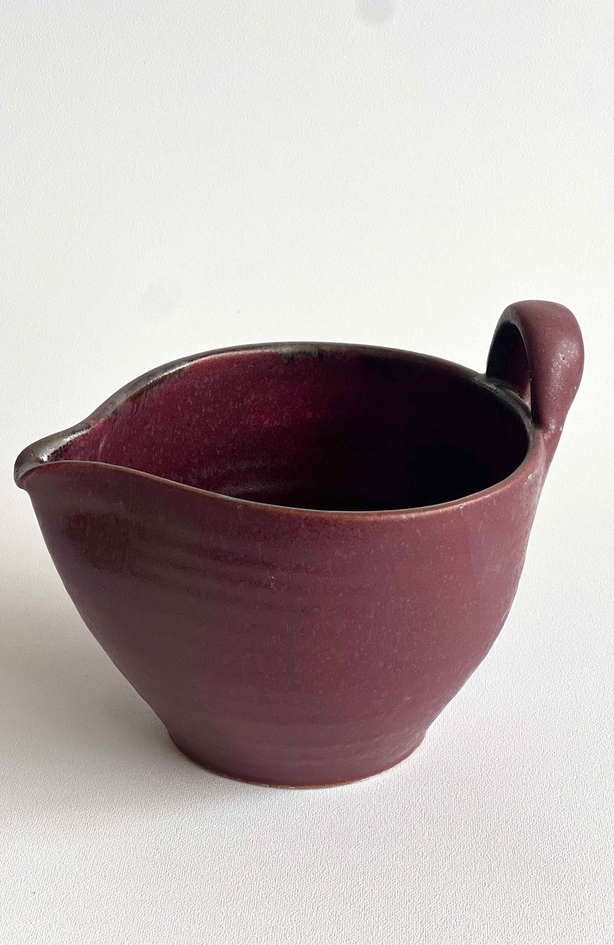 Burgundy stoneware batter bowl with side handle and glossy speckled interior