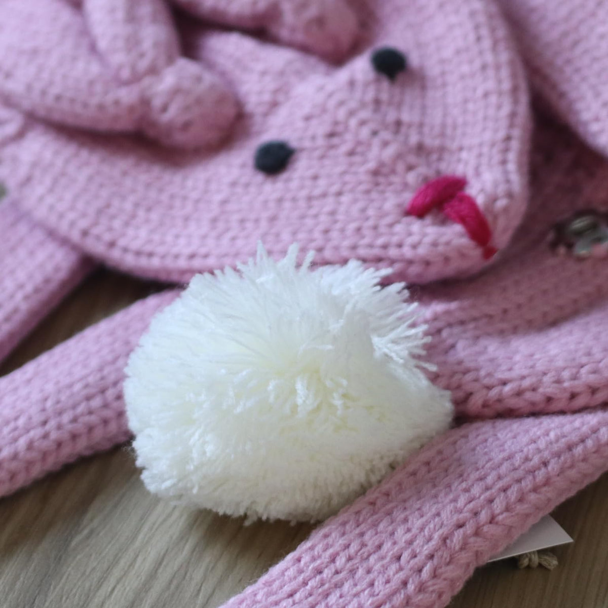 Pink knitted bunny scarf close-up with embroidered face and fluffy white pom-pom