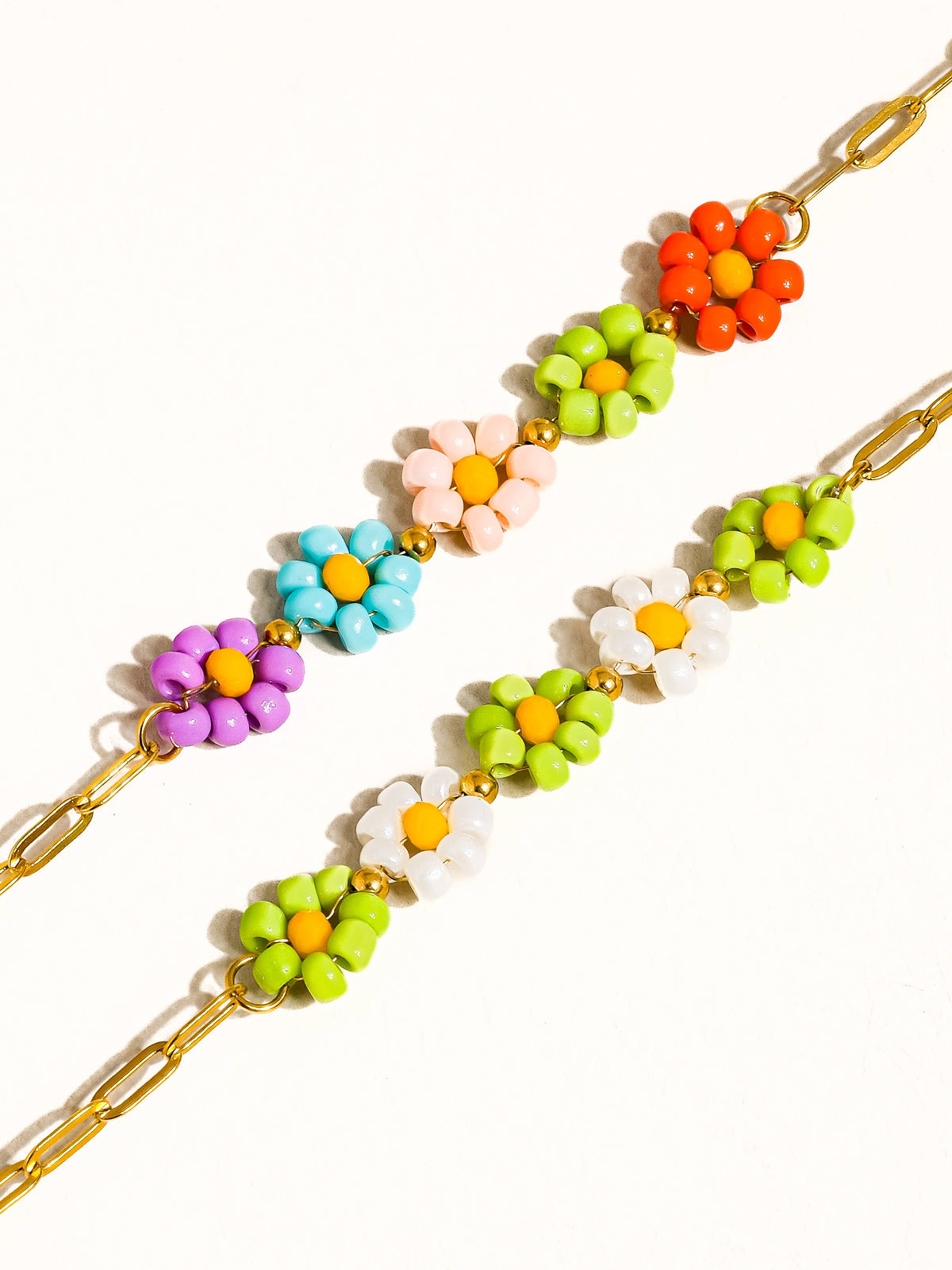 Close-up of a gold-tone chain bracelet with multicolored beaded daisy flowers.