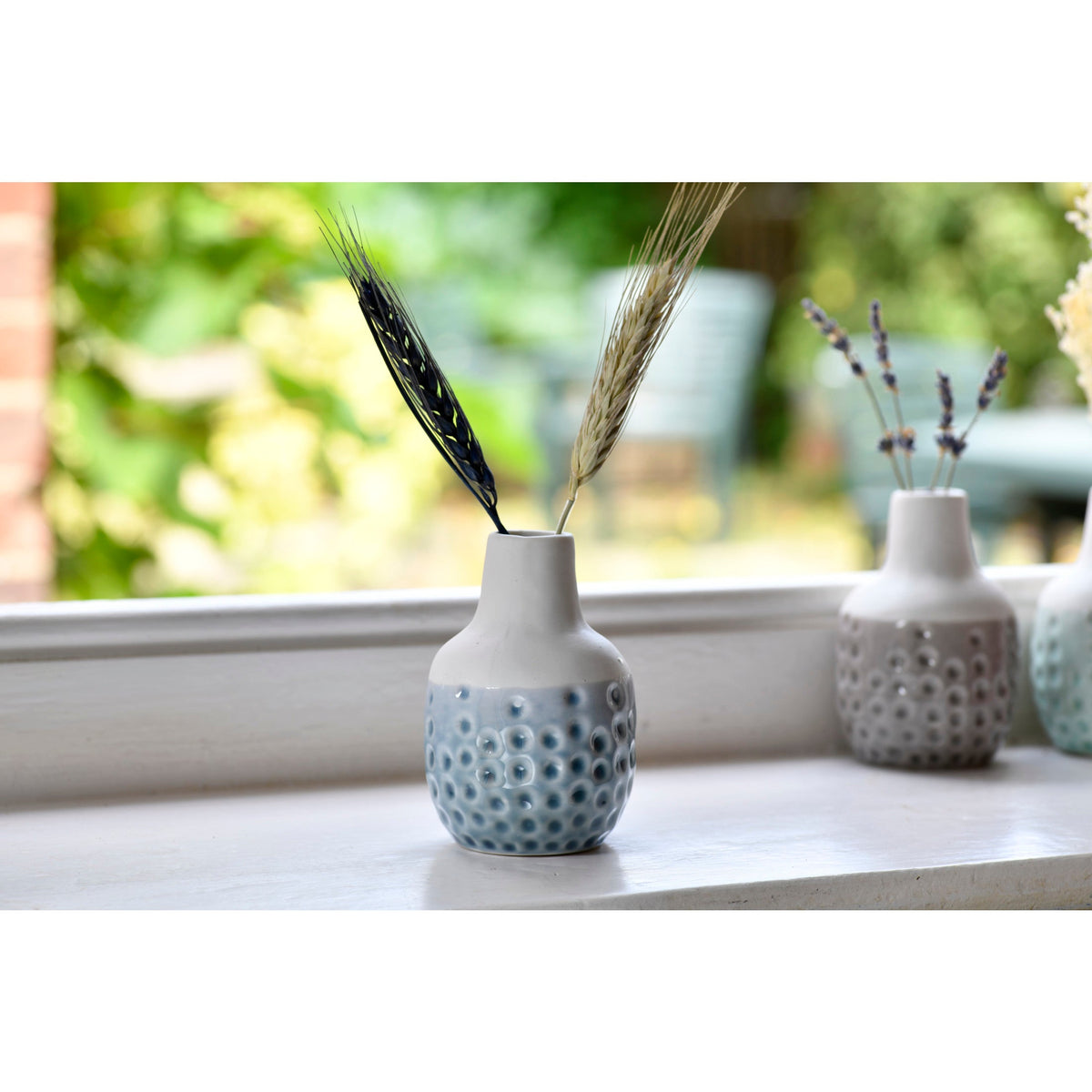 Mini ceramic dot vase with tall wheat stems, light blue speckled; other vases behind