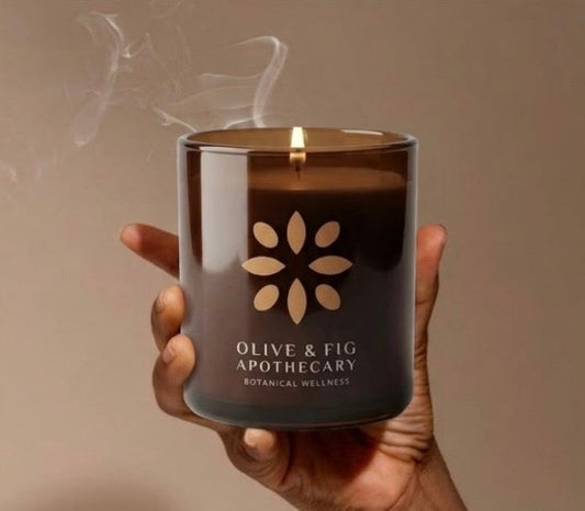 Lit amber glass jar candle with floral emblem, held in hands