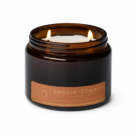 Amber glass candle jar with 'Smokin' Cowboy' label and two wicks burning