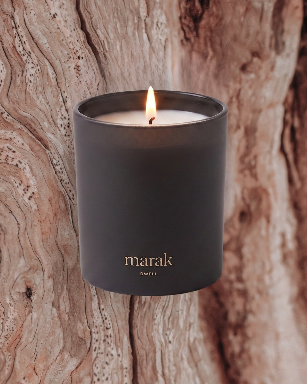 Lit marak candle in matte dark container, standing on wood surface