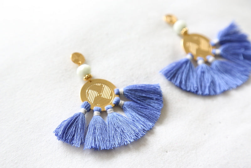 Close-up of blue tassel earrings with gold disc, white beads, and layered fringe