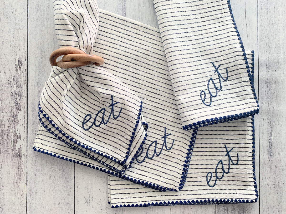 Wood napkin rings on striped cloth napkins with blue embroidered trim