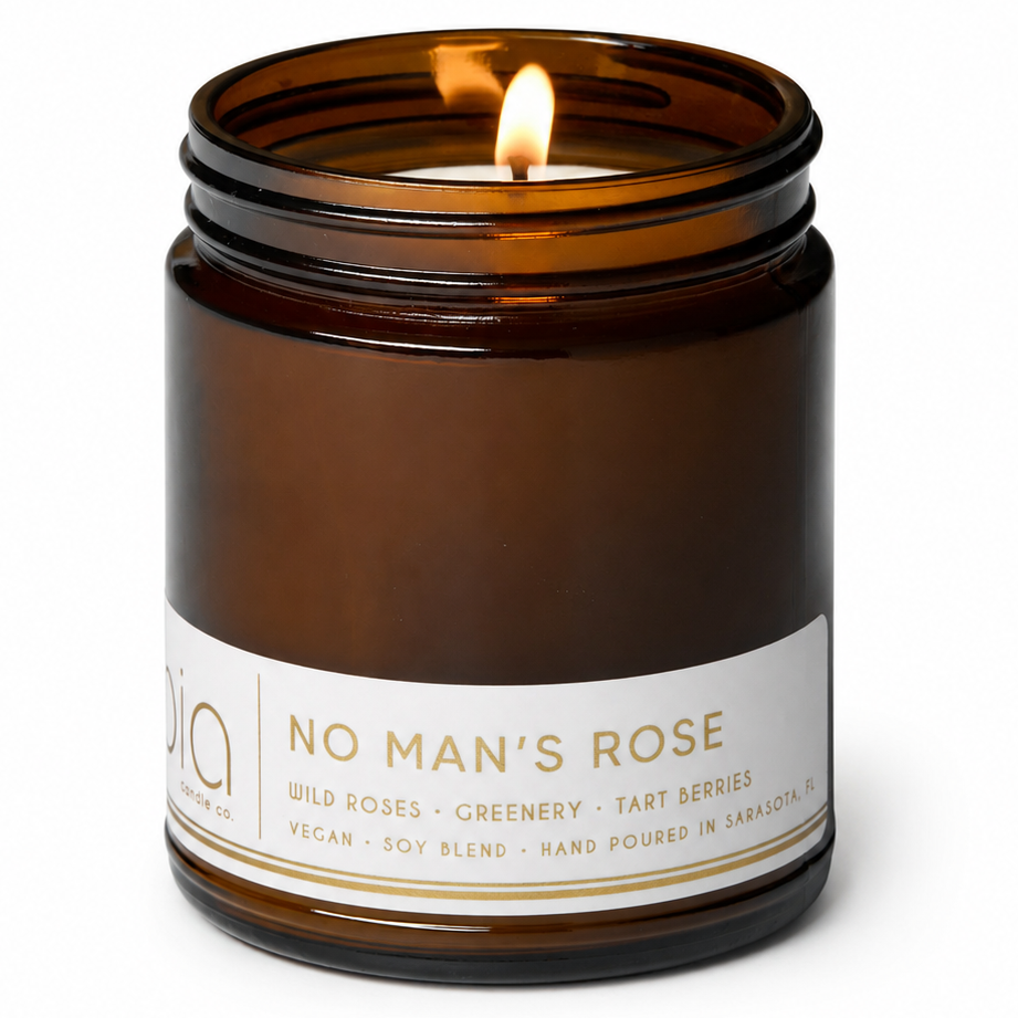 Brown amber candle jar with lit wick and printed label on the front