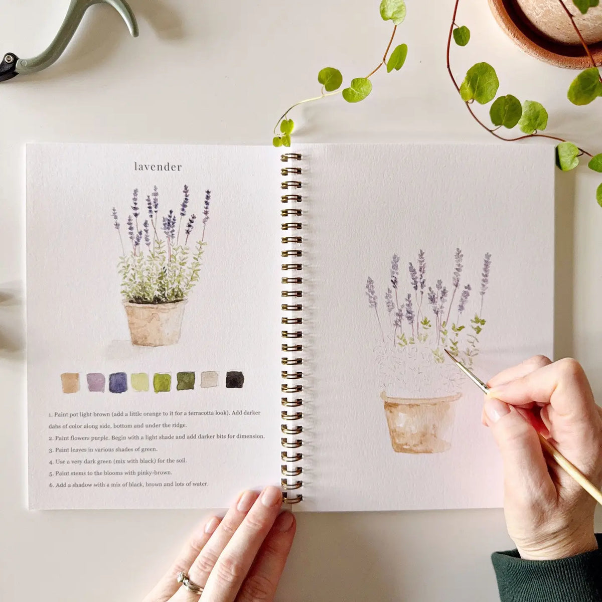 Garden watercolor workbook open to lavender page with painted flowers and color swatches
