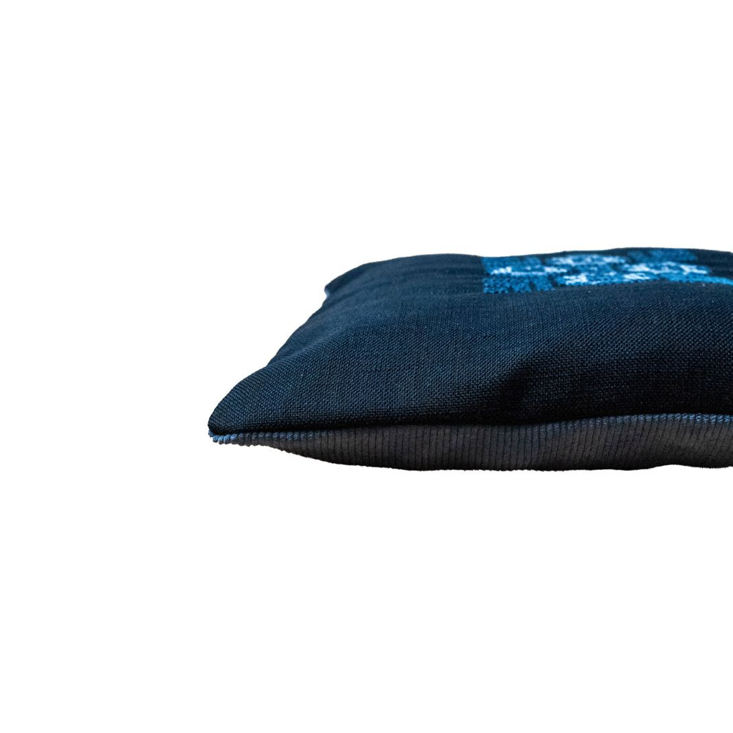 Blue pillow cover with visible folded edge and centered blue cross-stitch detail