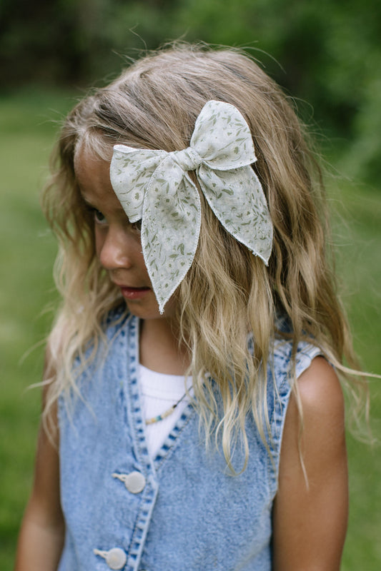 Girl wearing Eden Darling hair bow, off-white with green leaf pattern