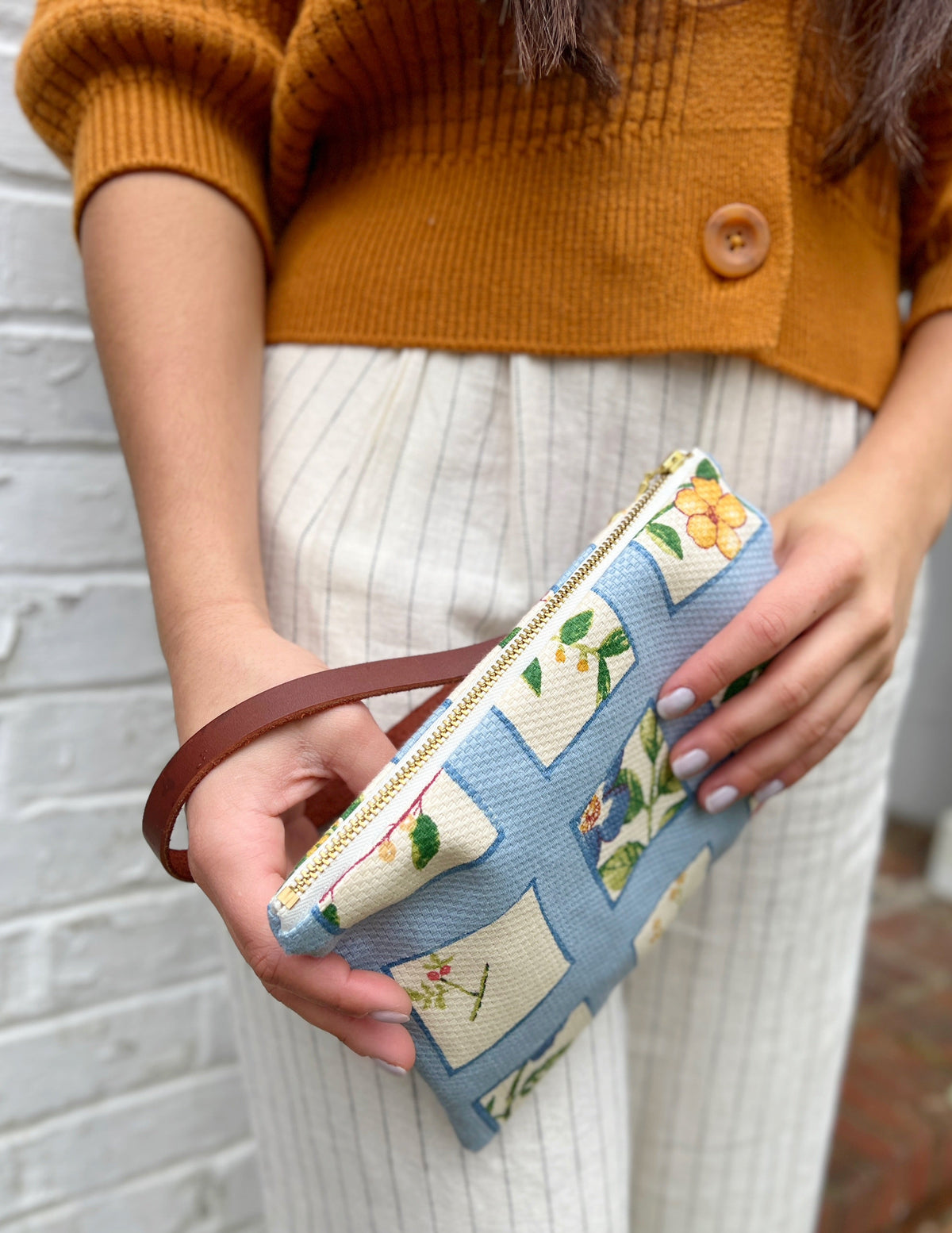 Blue patchwork wristlet purse held in hands, gold zipper and wrist strap