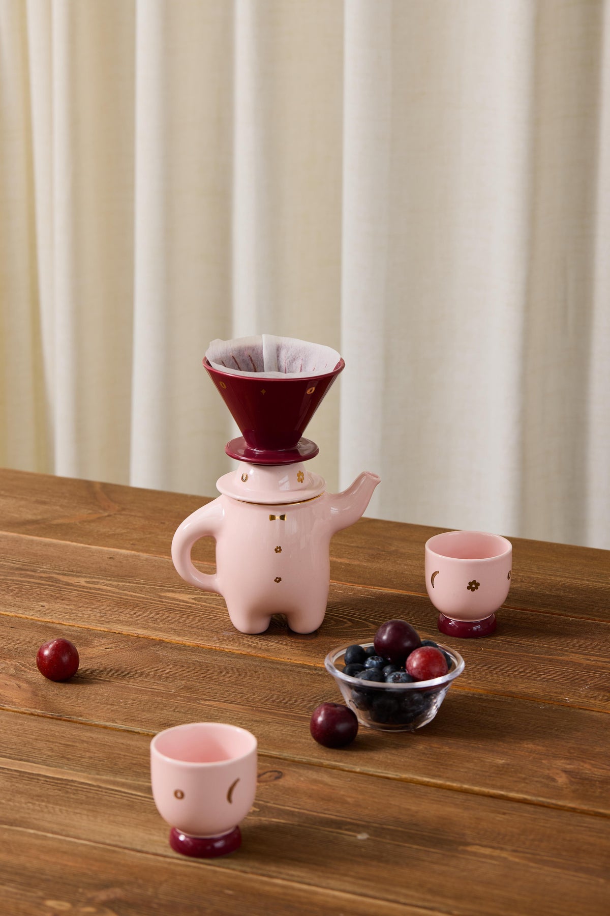Pink porcelain teapot on wooden table with coffee dripper and two matching cups