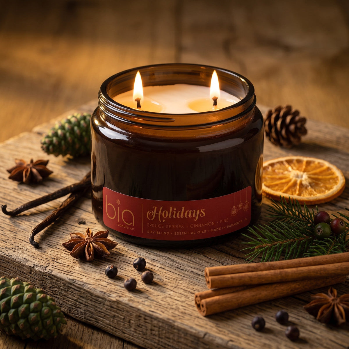 Amber glass soy candle jar with two flames and label, surrounded by spices and pine