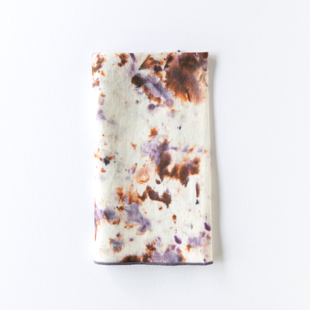 Marble-pattern napkin with white base and orange, purple, and brown splatter; dark border.