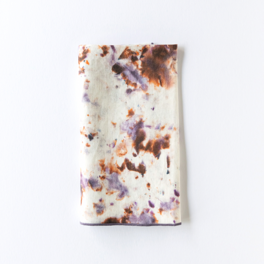 Marble-pattern napkin with white base and orange, purple, and brown splatter; dark border.