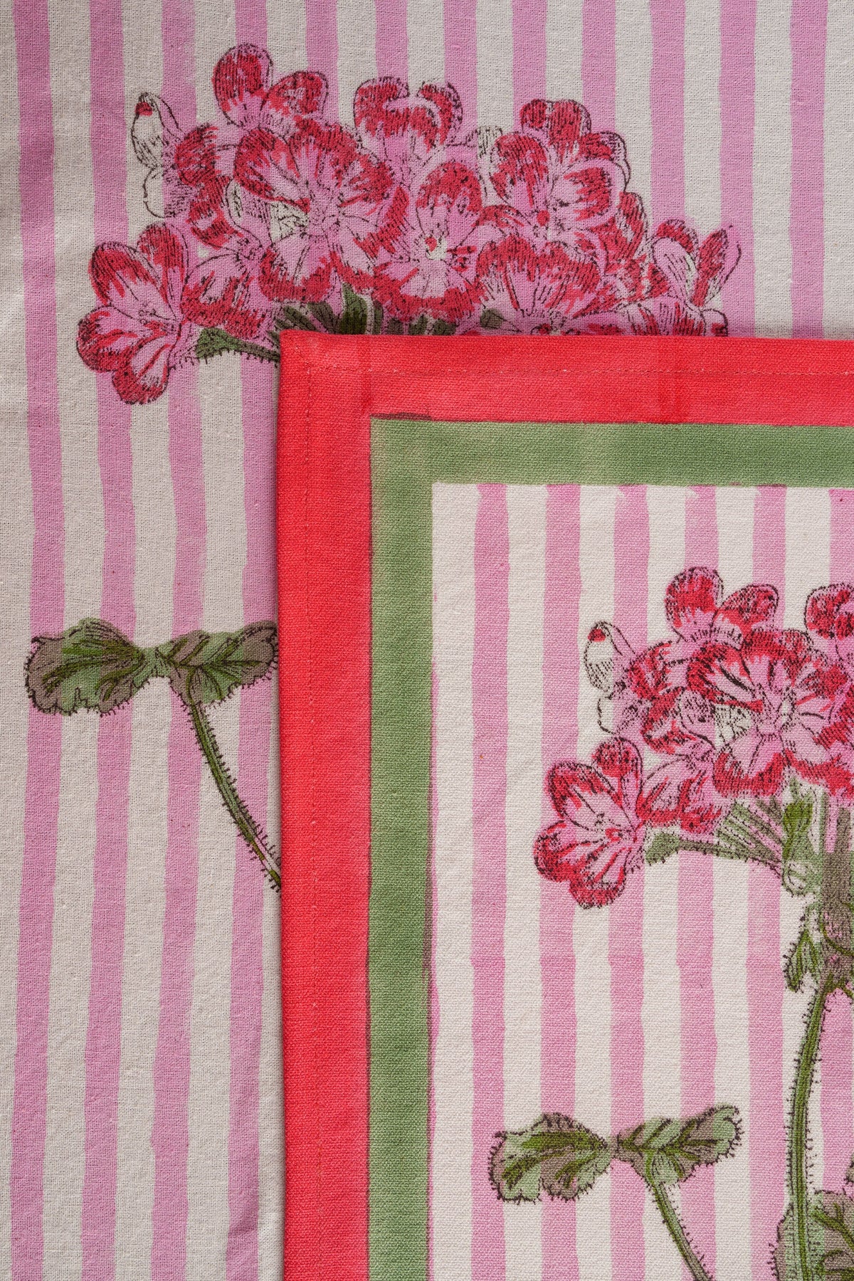 Close-up of pink hydrangea blockprint placemat edge with red border and vertical stripes