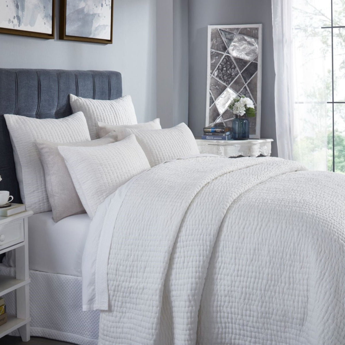 White quilt and matching shams on a bed, with visible textured stitched surface