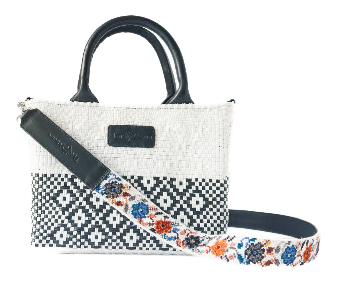 Small woven crossbody bag with black leather handles and floral strap on white and black pattern
