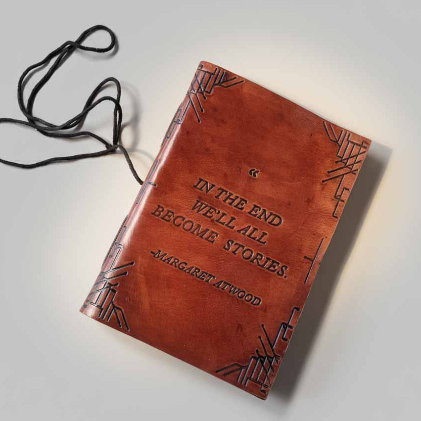 Brown leather journal with embossed border pattern and Margaret Atwood quote, tied with black cord