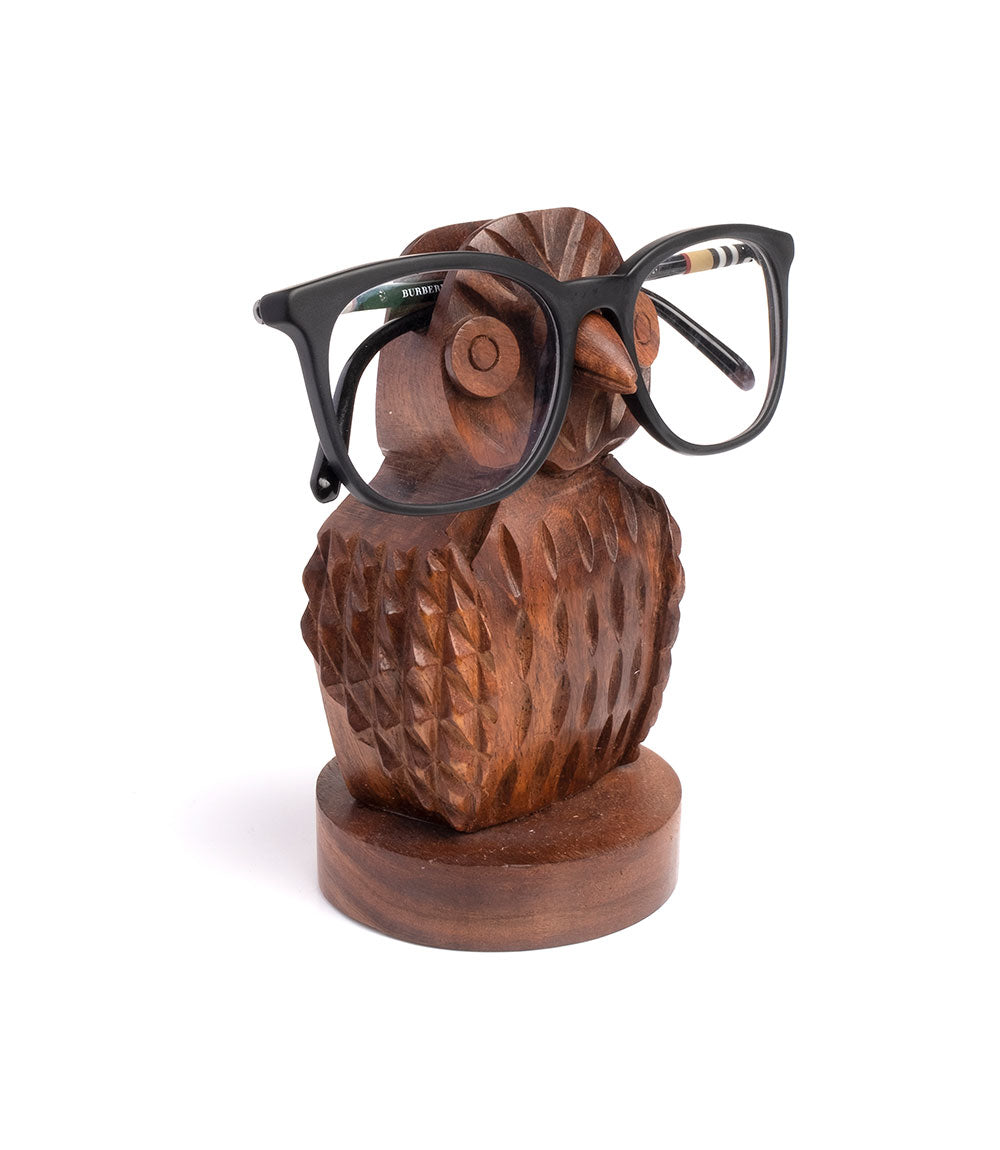 Hand-carved wooden owl eyeglass holder stand with black eyeglasses resting across the face.