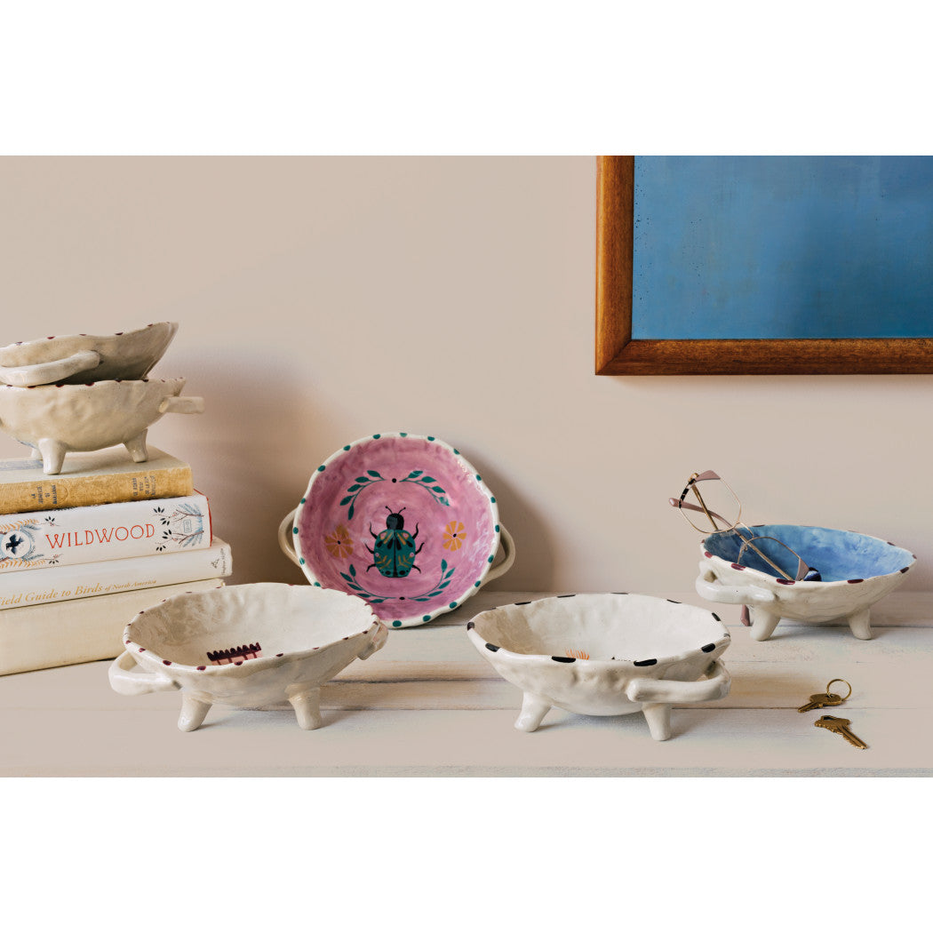 Set of footed bowls with colorful round designs and three short legs, cream bases.
