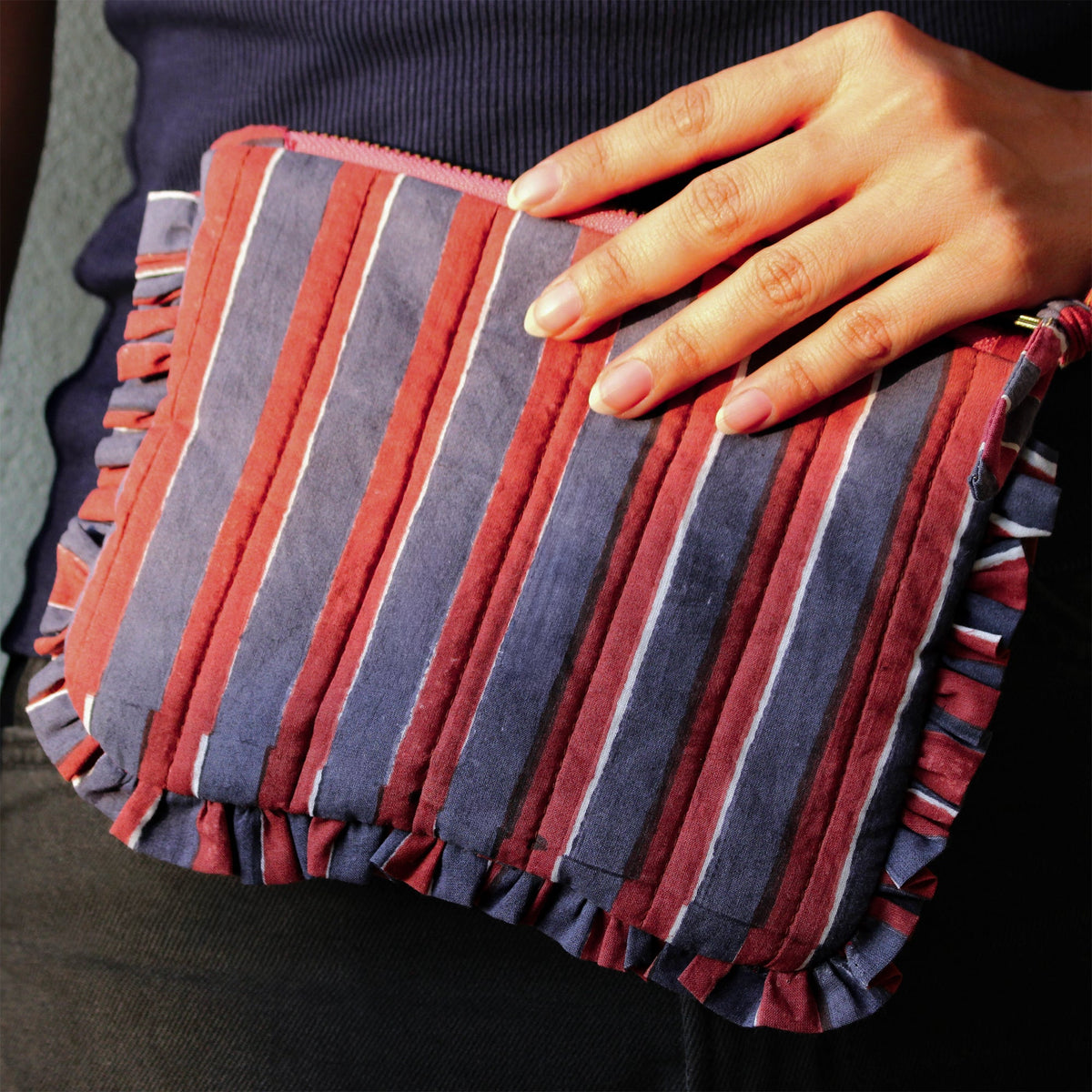 Striped quilted travel pouch with frill trim and zip top, held in hand