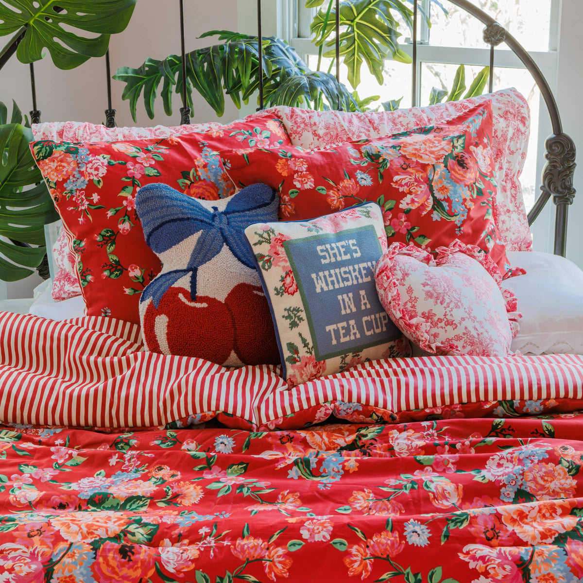 Embroidered decorative pillow with “She’s Whiskey in a Tea Cup” on red floral quilt