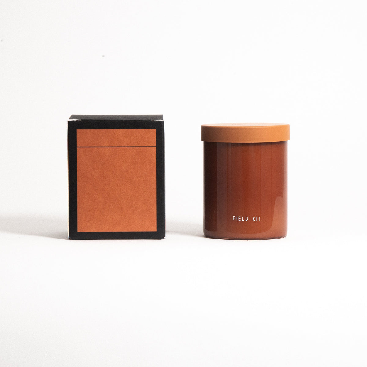 Scented candle in amber jar with orange lid beside square product box