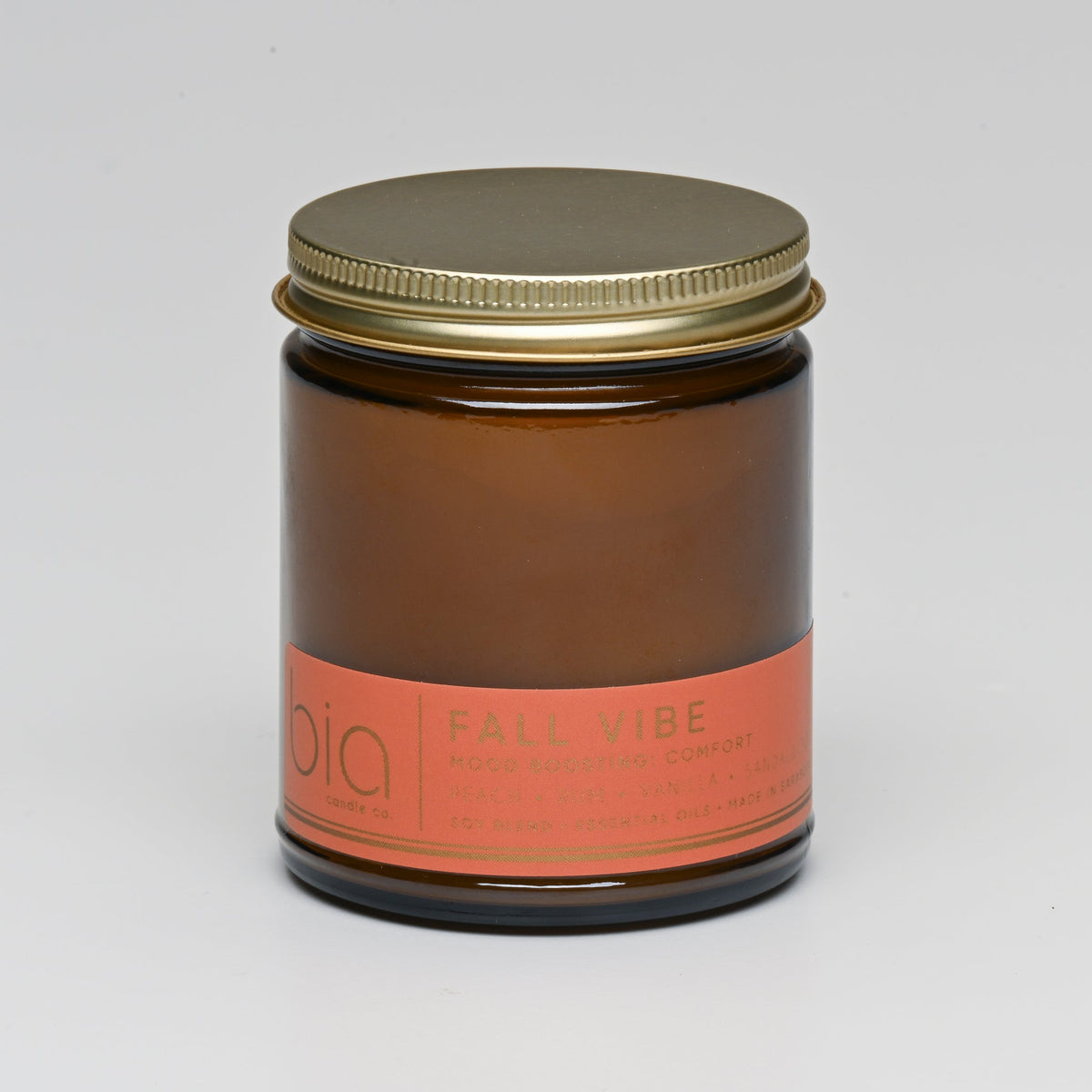 Amber glass candle jar with metal lid, orange label on front