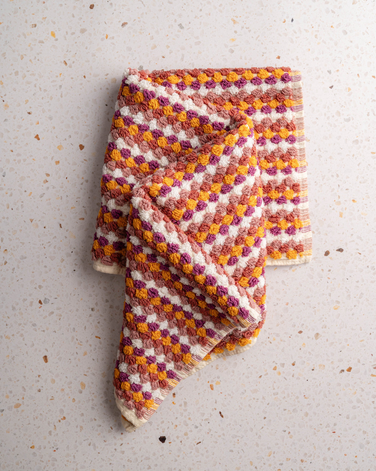 Checkered hand towel in plum, orange, and cream tones, no tassels, folded corner-up.