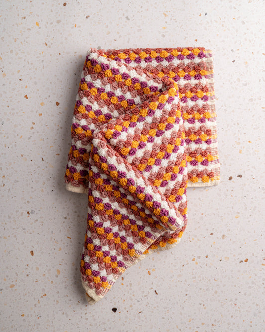 Checkered hand towel in plum, orange, and cream tones, no tassels, folded corner-up.