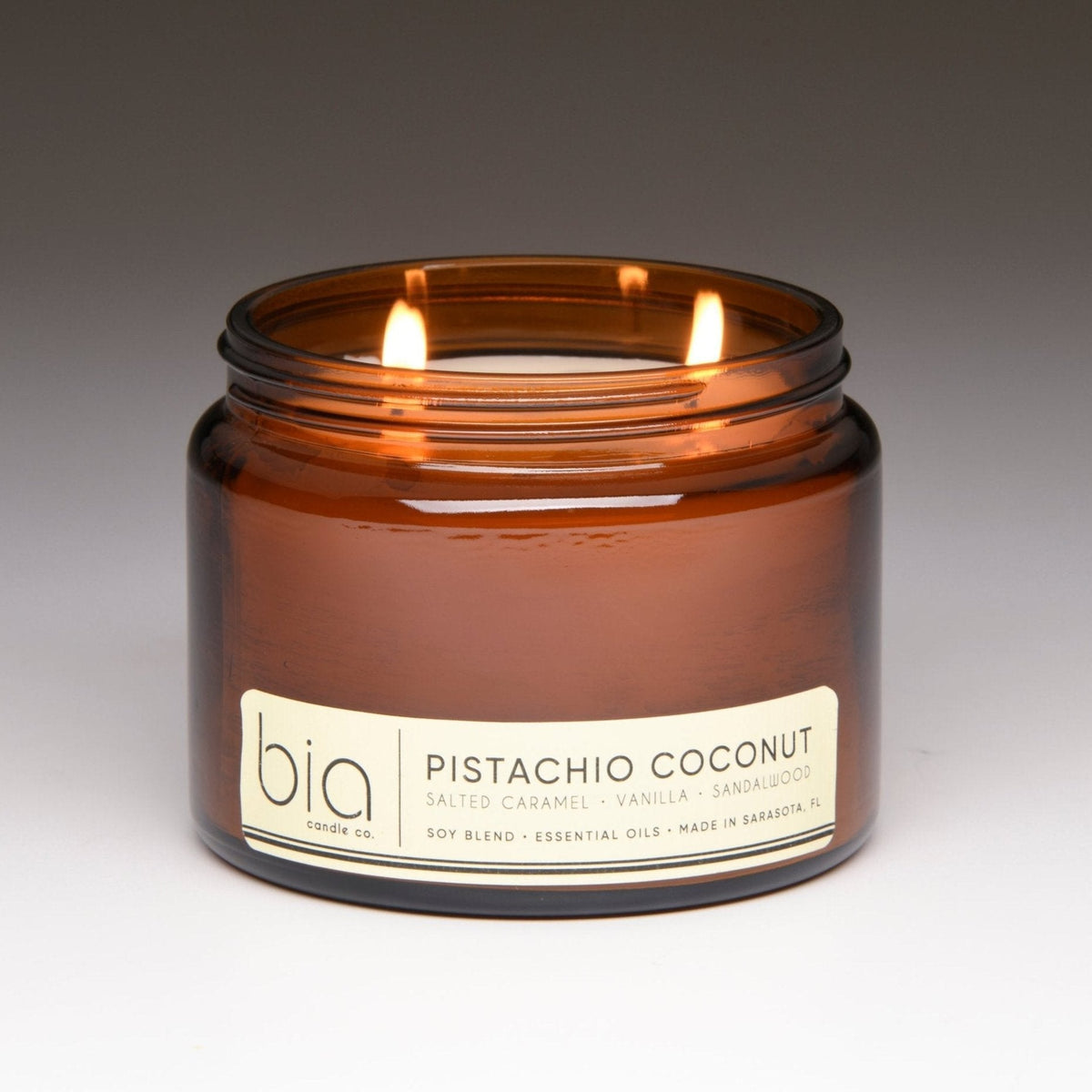 Amber glass candle jar with two lit wicks, “Pistachio Coconut” label