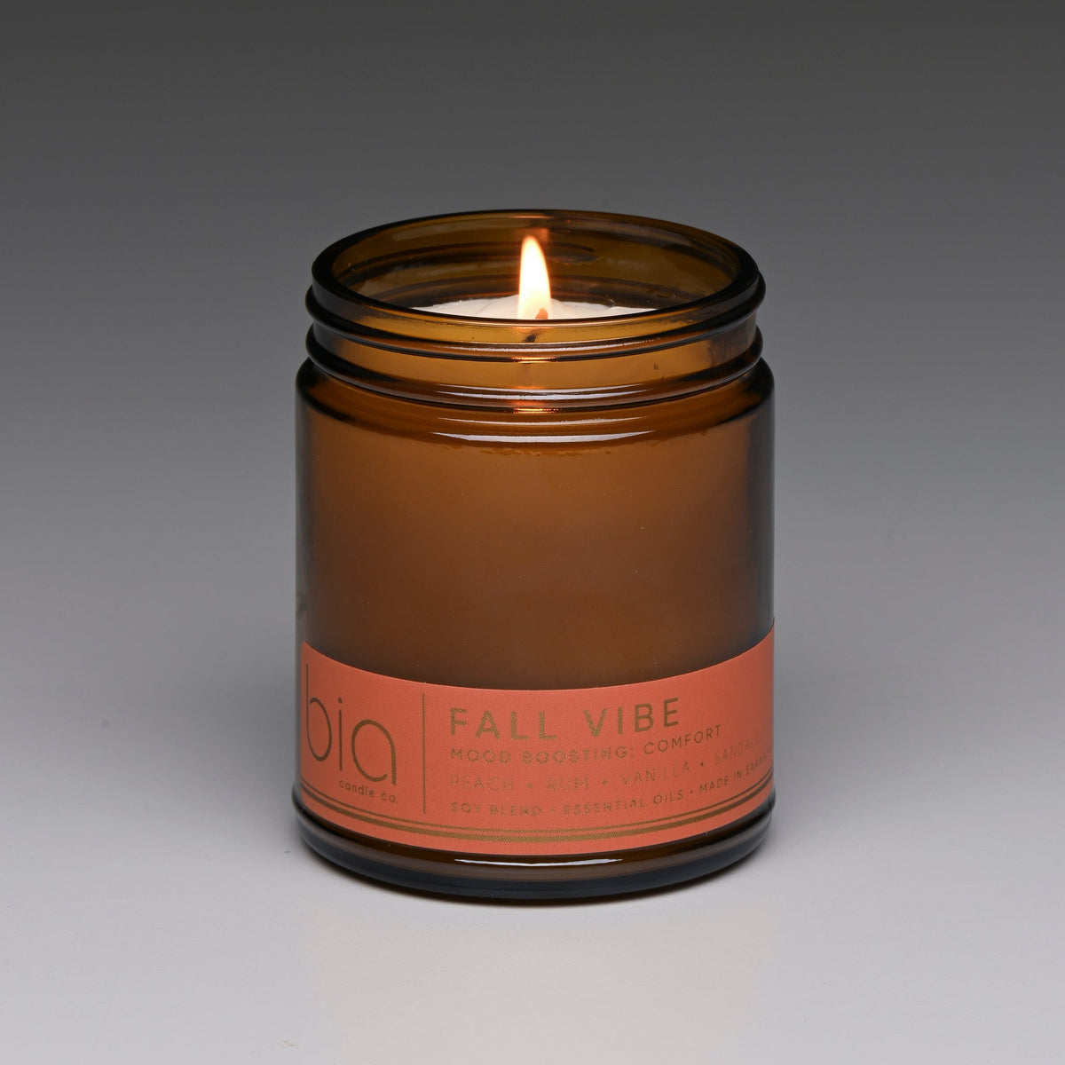 Amber soy candle in glass jar with lid ring, lit wick, orange front label