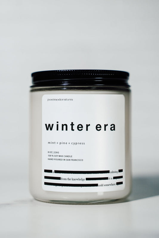 Scented candle jar with white 'winter era' label and black lid