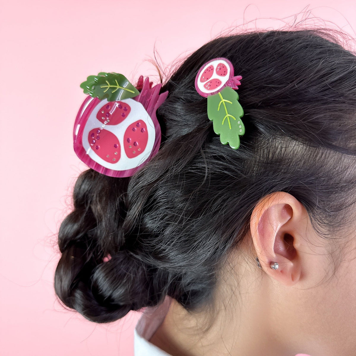 Pomegranate-themed hair claw clipped in dark hair, showing red fruit and green leaf accents
